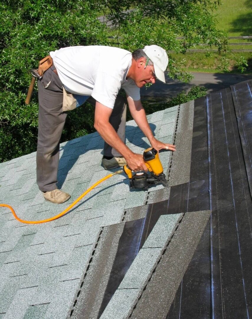 Man uses nail gun to apply asphalt shingles to roof