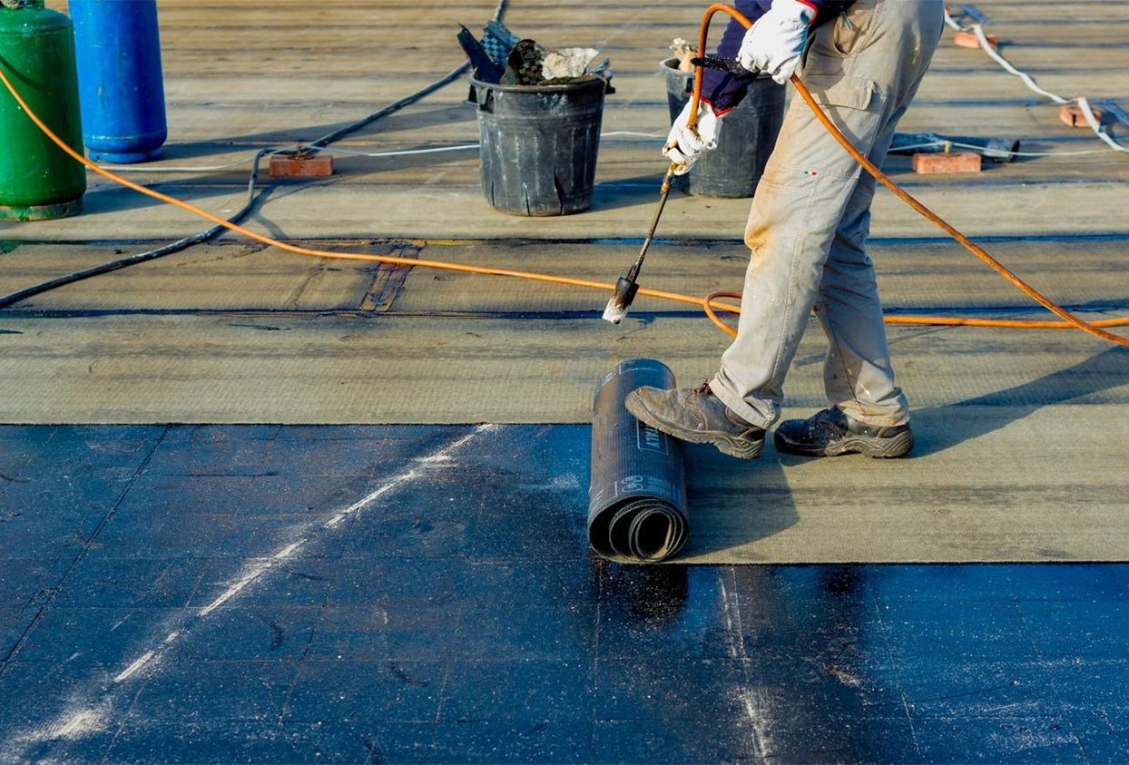 Worker preparing part of bitumen roofing felt roll for melting by gas heating burner flame